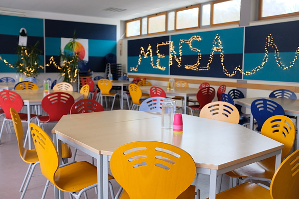 Mensa - Raum mit Tischen, bunten Stühlen und einer Lichterkette mit dem Schriftzug Mensa im Hintergrund